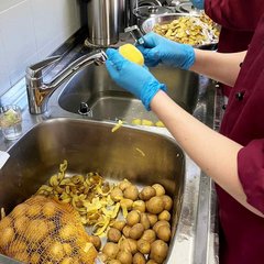 Bild von vier Händen beim Kartoffelschälen in der Produktionsküche der Diakonie-Werkstatt.