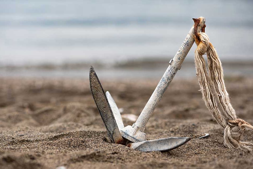 Symbolbild. Ein Anker, der im Sand am Strand liegt.