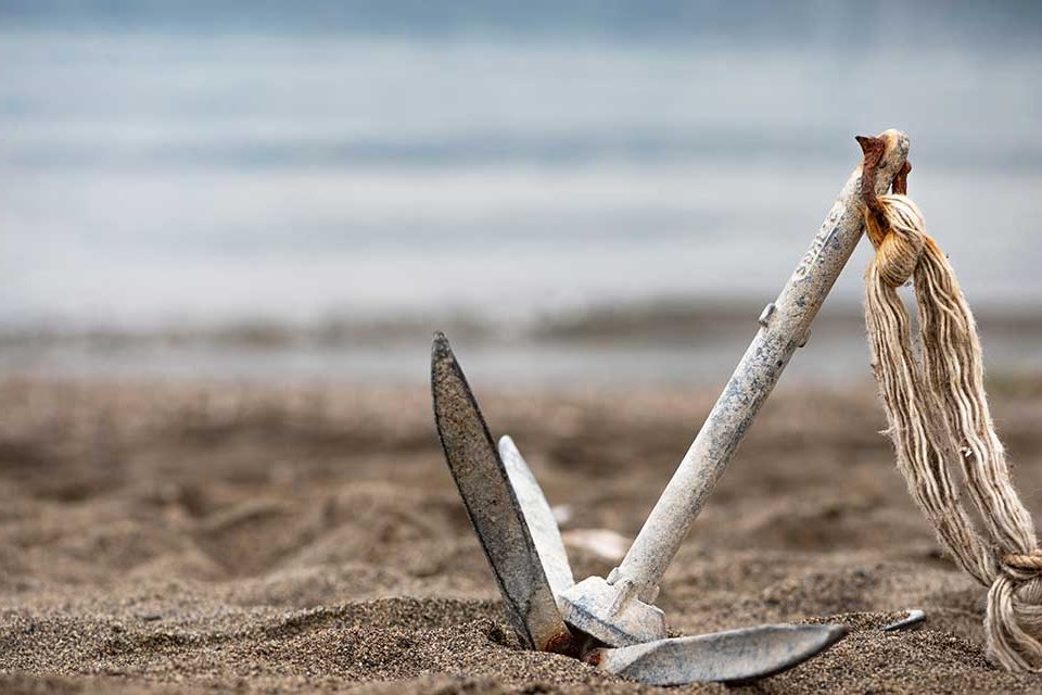 Symbolbild. Ein Anker, der im Sand am Strand liegt.