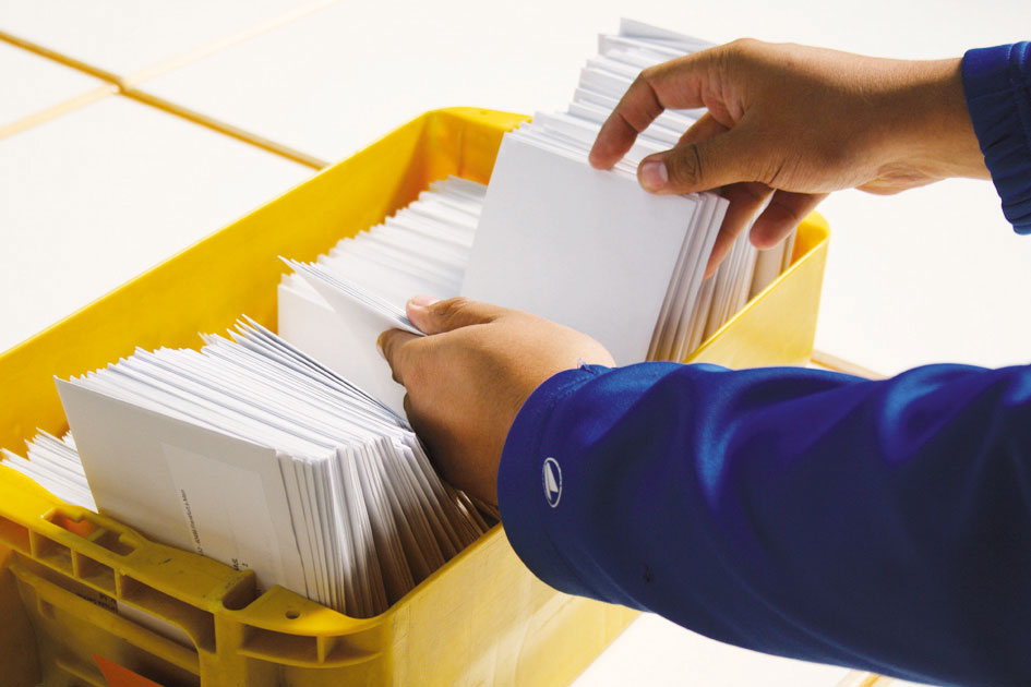 Bild mit den Händen einer Person, die in einer Kiste Briefumschläge sortiert.